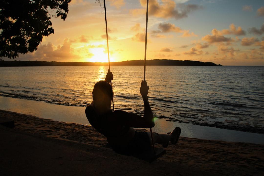 silhouette of woman sitting on swing near body of water during sunset