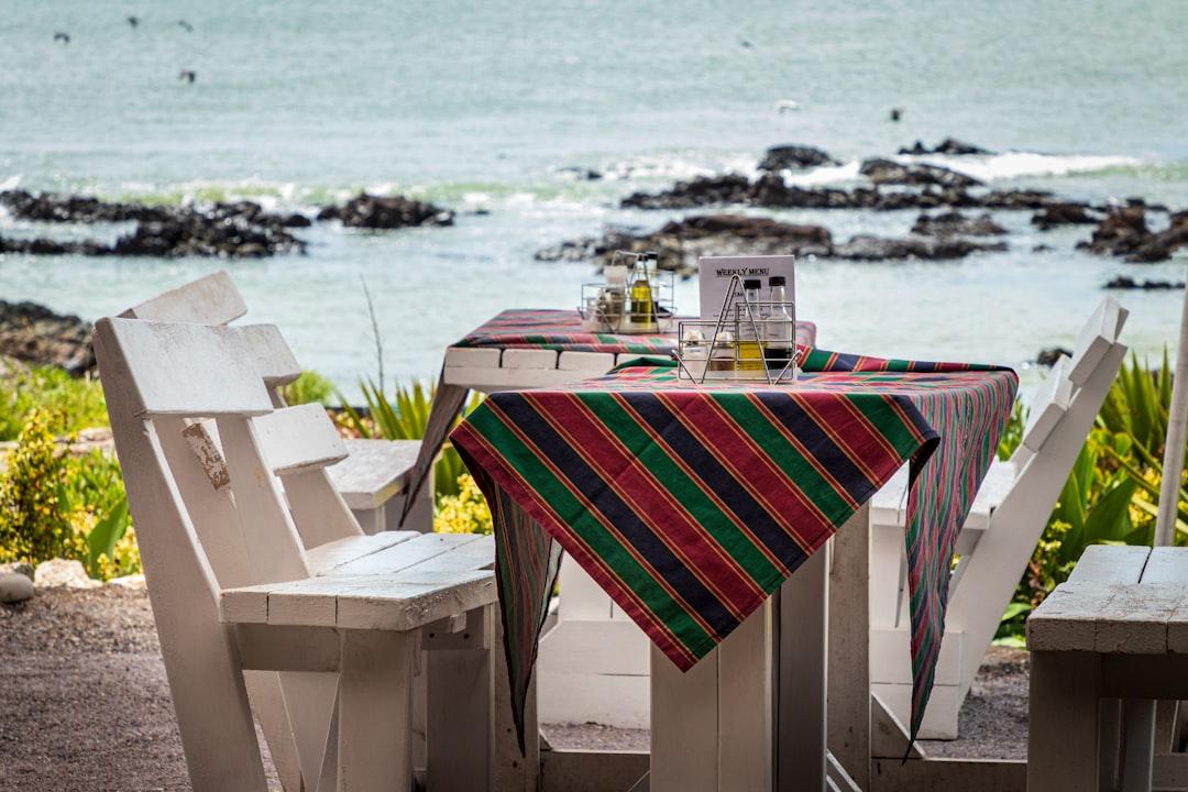 Restaurant table with table cloths and condiments with the ocean in the background 