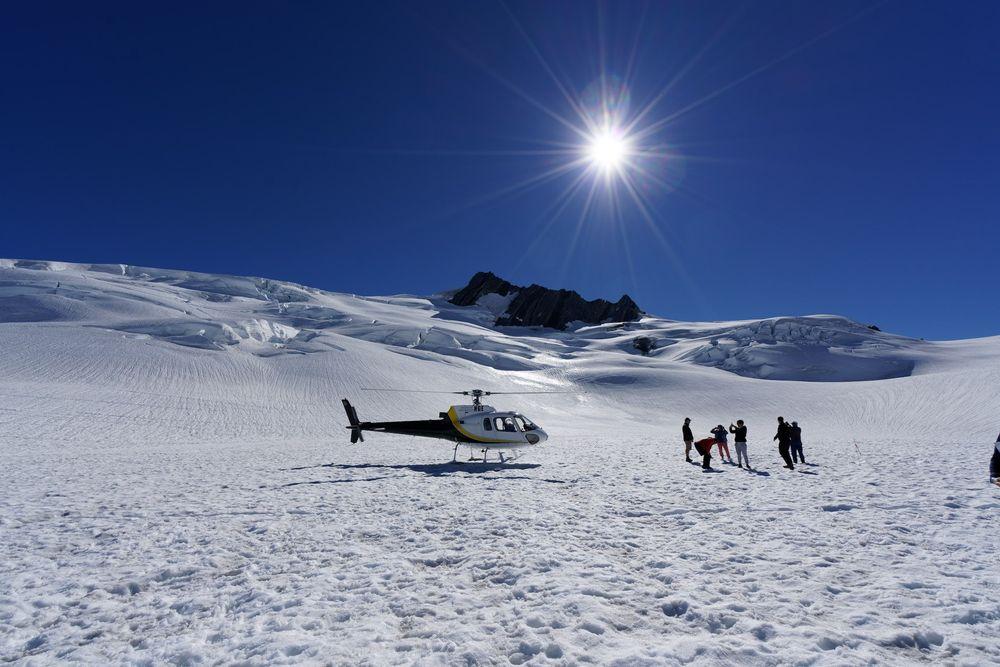 A helicopter trip to the Fox Glacier in New Zealand. Image on the glacier with helecopter and people with backlit sun on the glacier.