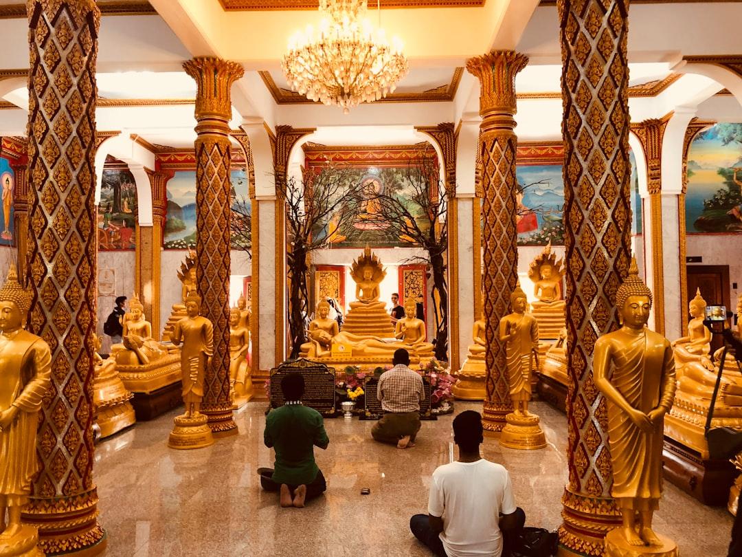 People praying inside Thai Buddhist temple with gold accent.